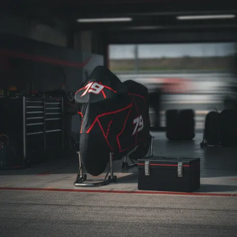 An empty MotoGP pit garage with a lone motorcycle under a cover, signifying a rider's absence from the race weekend.