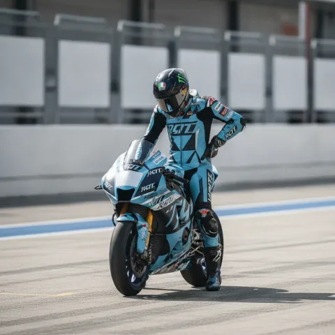 A MotoGP rider on a light blue and red motorcycle leans at an extreme angle while cornering on a race circuit.