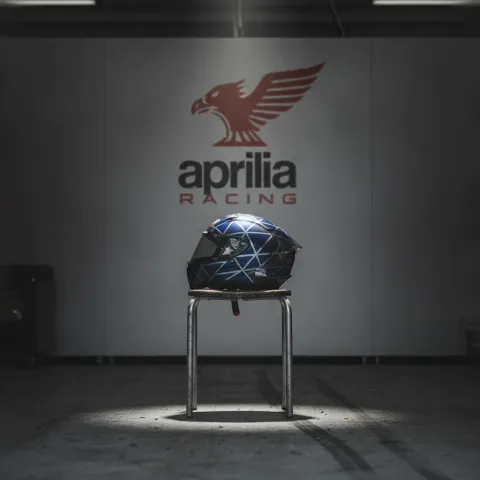 A lone racing helmet rests on a stool in an otherwise empty and quiet MotoGP pit garage, signifying a rider's absence due to injury.