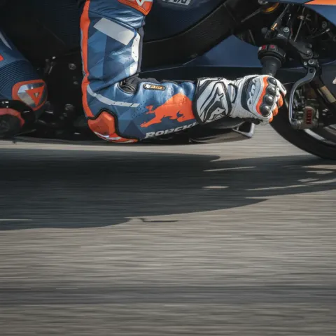 A close-up view of a MotoGP rider's arm and gloved hand, showing the extreme muscle tension required to control the bike.