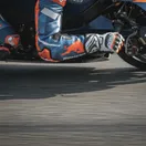 A close-up view of a MotoGP rider's arm and gloved hand, showing the extreme muscle tension required to control the bike.