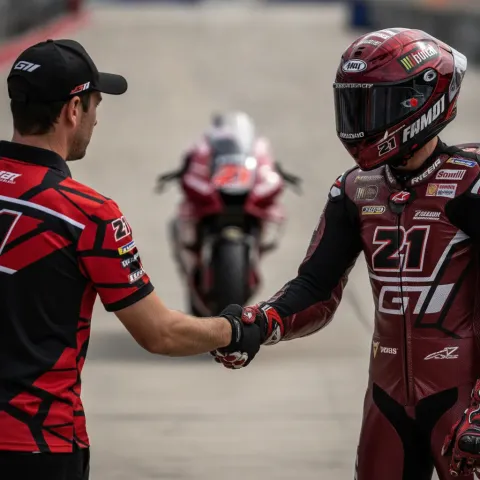 A team manager and a MotoGP rider shaking hands in the pit lane, signifying a future departure from the team.
