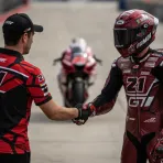 A team manager and a MotoGP rider shaking hands in the pit lane, signifying a future departure from the team.