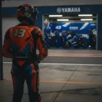 A MotoGP rider in orange leathers contemplates a move to a rival manufacturer's blue-liveried team.