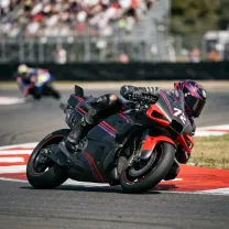 A MotoGP racer leans dramatically into a turn with an elbow skimming the kerb.