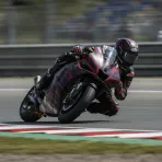 Marco Bezzecchi leans his Aprilia race bike at an extreme angle through a corner during a MotoGP race.