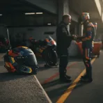 A rider's helmet sits on a pit wall, with the out-of-focus shape of a person in the garage behind, symbolising mentorship in MotoGP.