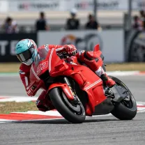 A MotoGP rider leaning at an extreme angle through a fast corner with elbow grazing the kerb.