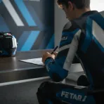 A young rider signs a contract at a desk, securing his future move to a top-level MotoGP team.