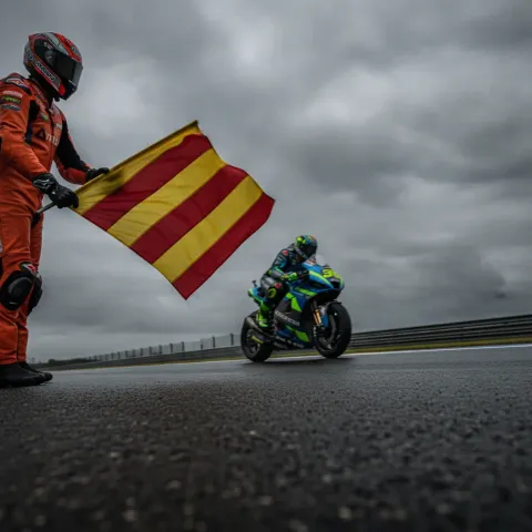 A marshal at a MotoGP circuit waves the yellow and red striped flag to warn of a slippery track surface.