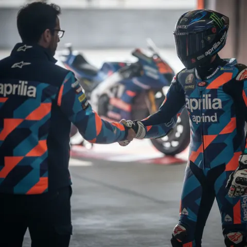 A rider and a team manager shaking hands in a MotoGP pit garage to signify a new contract agreement.