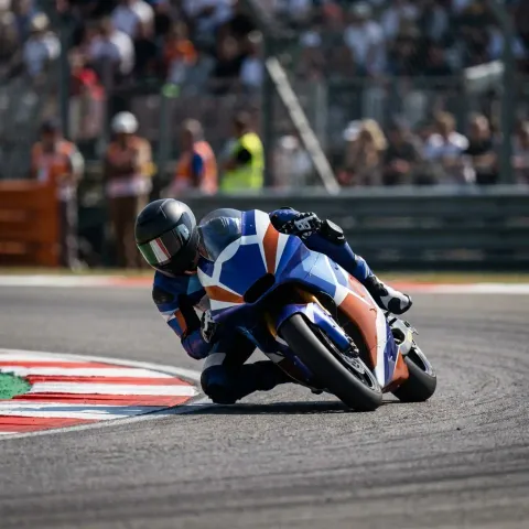 A pack of MotoGP motorcycles leaning hard into the first corner during a frantic Sprint race.