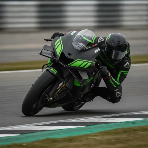 A MotoGP test rider leans at an extreme angle through a corner on a prototype motorcycle with a matte black and green livery.